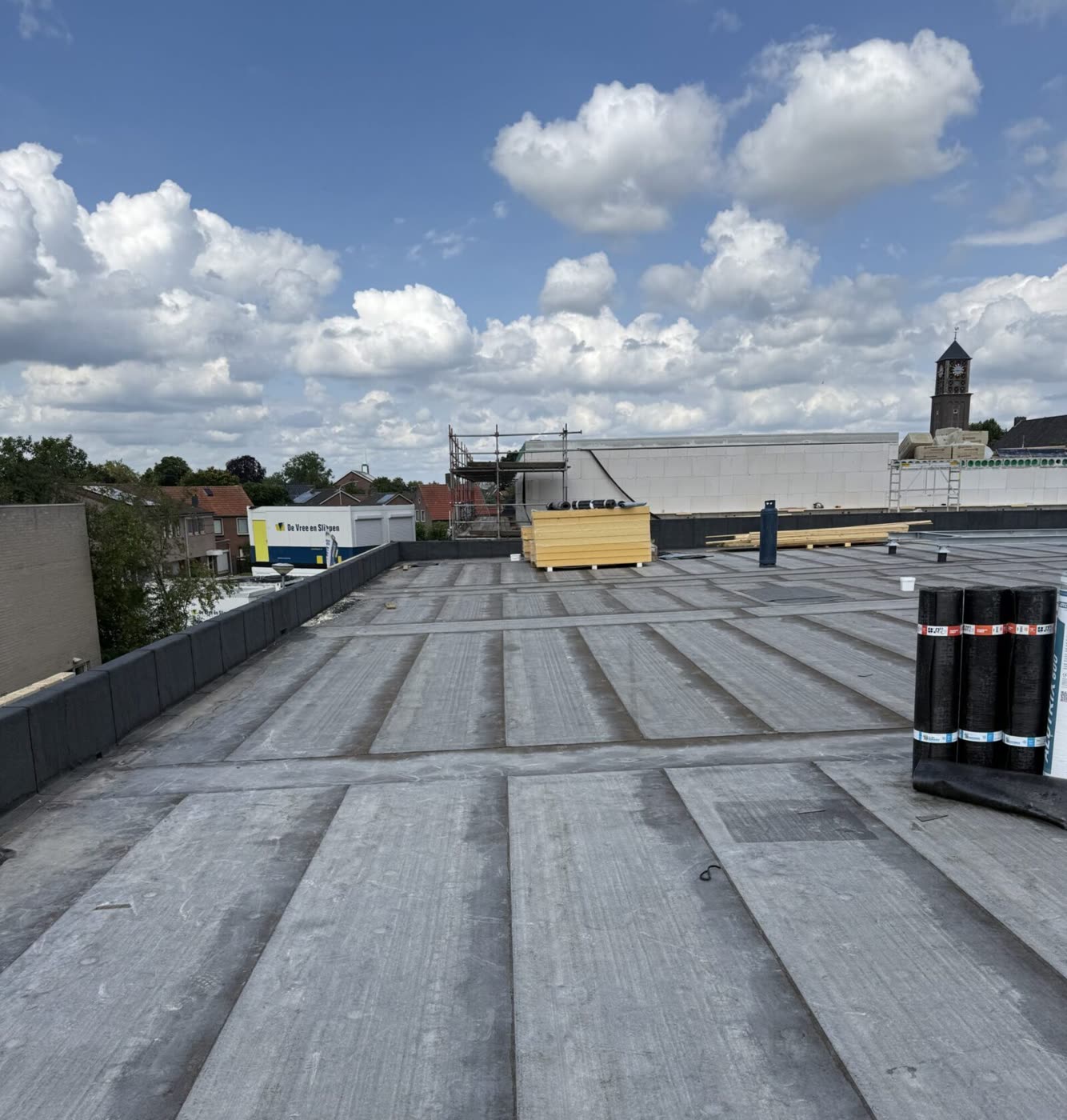 Plat dak in aanbouw met een Hollandse wolkenlucht en een kerktoren op de achtergrond